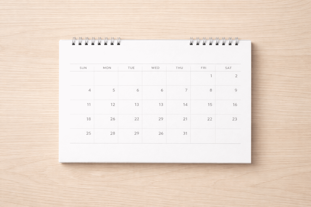 木製テーブルに平置きされた卓上カレンダーを上から撮影した写真。シンプルな月間カレンダーのデザイン。
