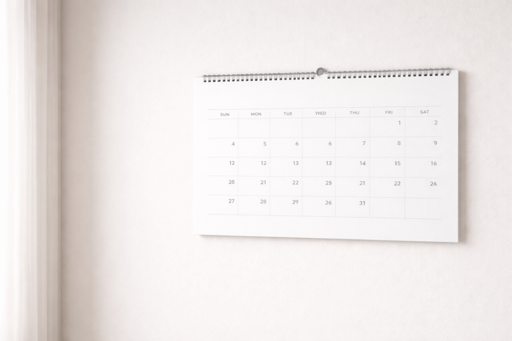 白い壁に掛けられたシンプルなデザインの壁掛けカレンダーの写真。月間カレンダーが表示されている。